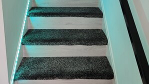Una escalera con peldaños alternados en blanco y negro, iluminada por luces LED azules a lo largo de la barandilla.
