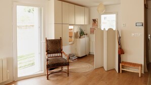 Une pièce dotée d’un plancher en bois, d’une chaise avec un coussin à motifs, d’un banc, d’une porte avec une poignée décorative et d’un mur orné d’œuvres d’art encadrées.