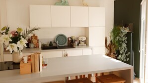 Une cuisine moderne avec des meubles blancs, un îlot central doté de tabourets et des éléments décoratifs, notamment un vase de fleurs et une assiette en céramique verte.