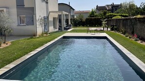 Une piscine rectangulaire à l’eau claire, entourée d’une pelouse bien entretenue et d’un mur de pierre.