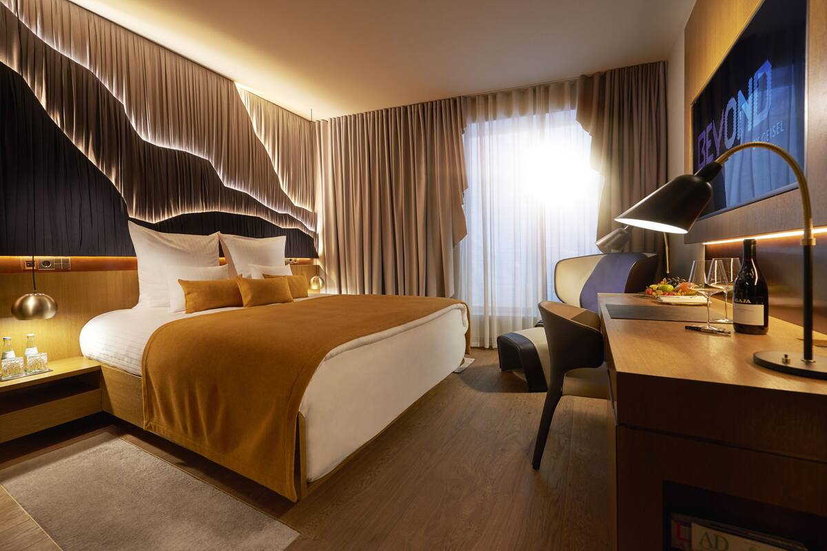 Et hotelværelse med en stor seng, et skrivebord med lampe, og udsigt til det fri gennem vinduet.