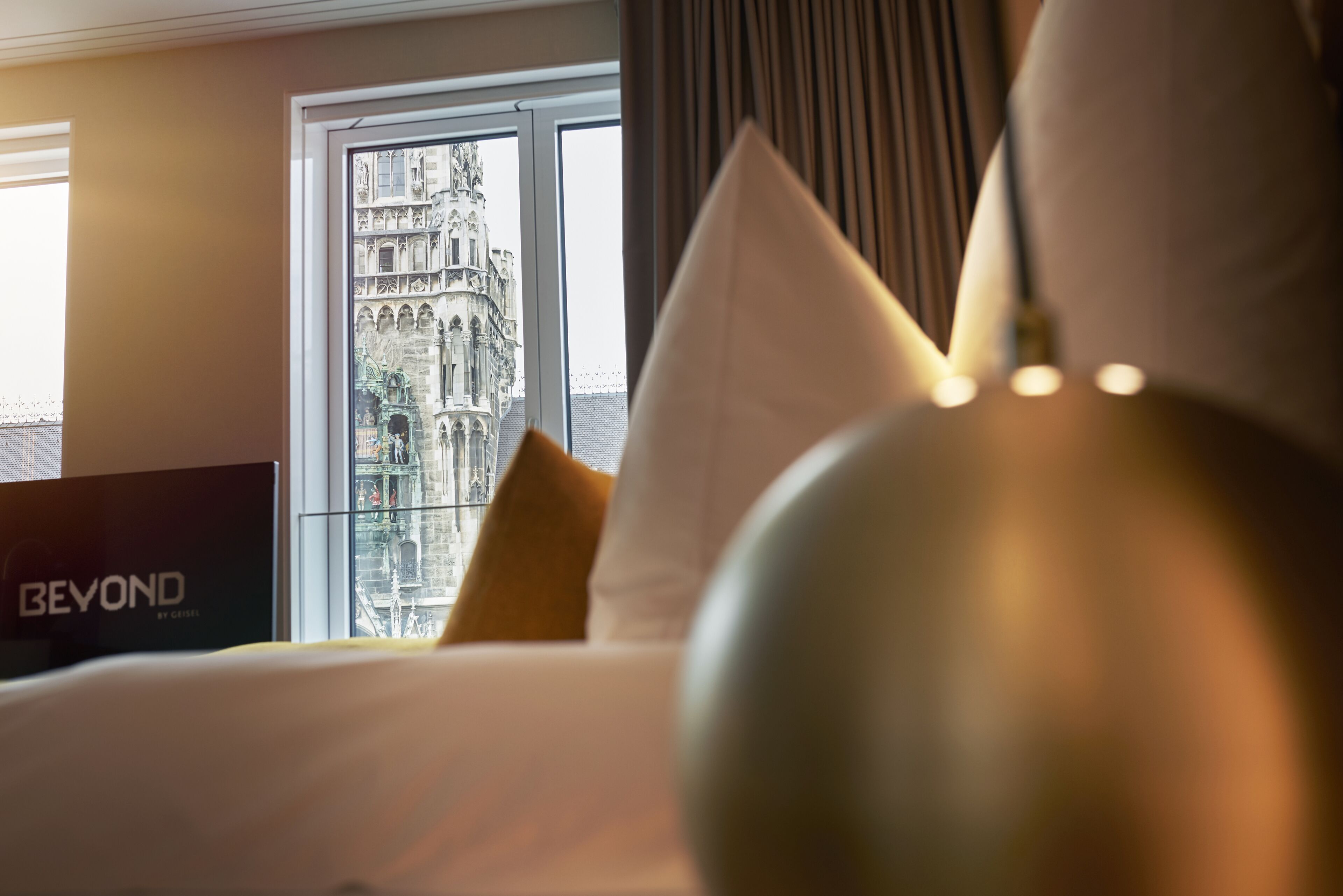 A hotel room with a bed, a view of a historic building through a window, and a sign reading "BEYOND".