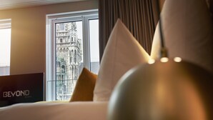 A hotel room with a bed, a view of a historic building through a window, and a sign reading "BEYOND". - BEYOND by Geisel (Munich)