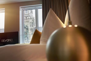 A hotel room with a bed, a view of a historic building through a window, and a sign reading "BEYOND".