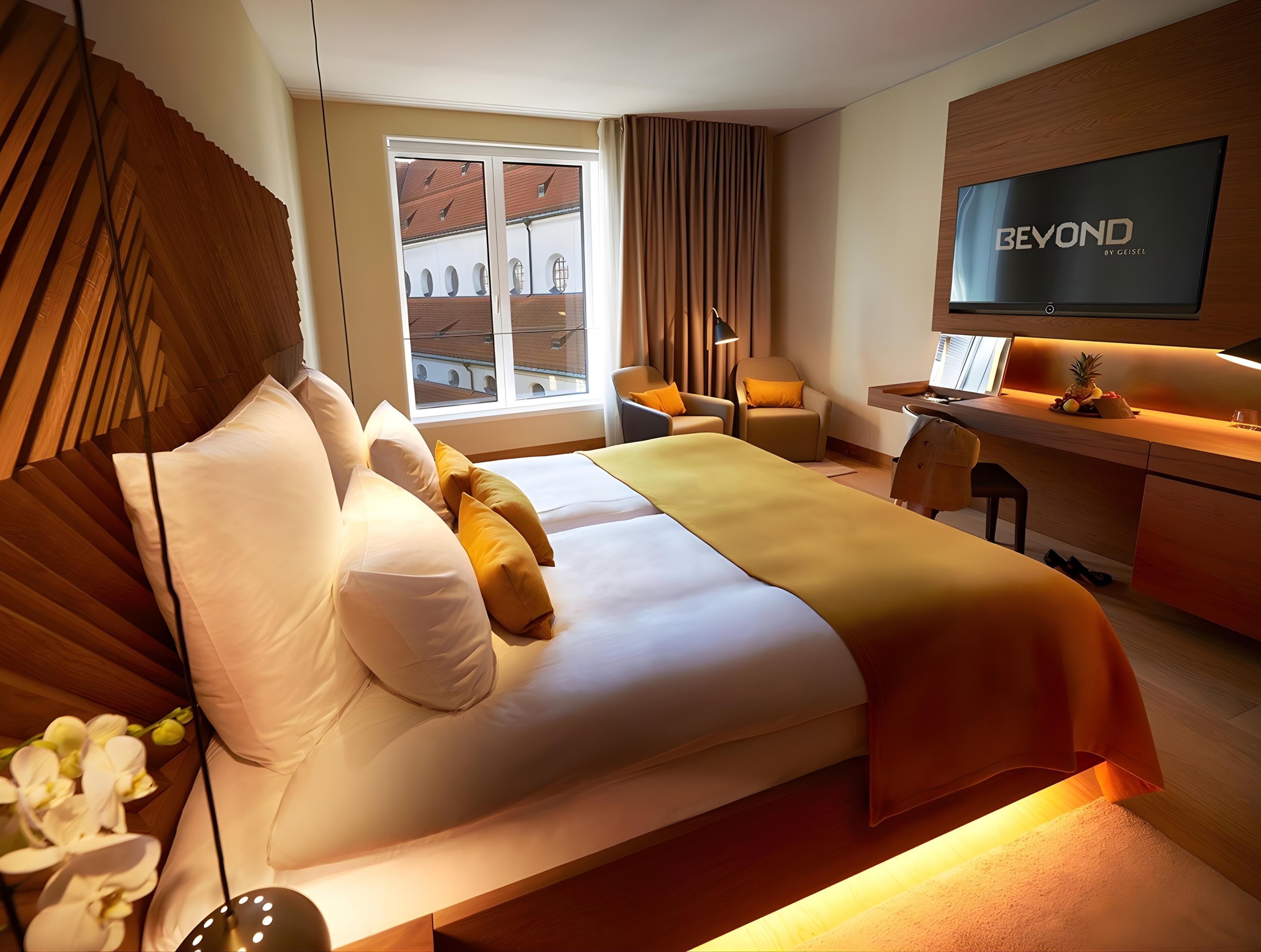 Una habitación de hotel con cama, escritorio, televisor y ventana con cortinas.