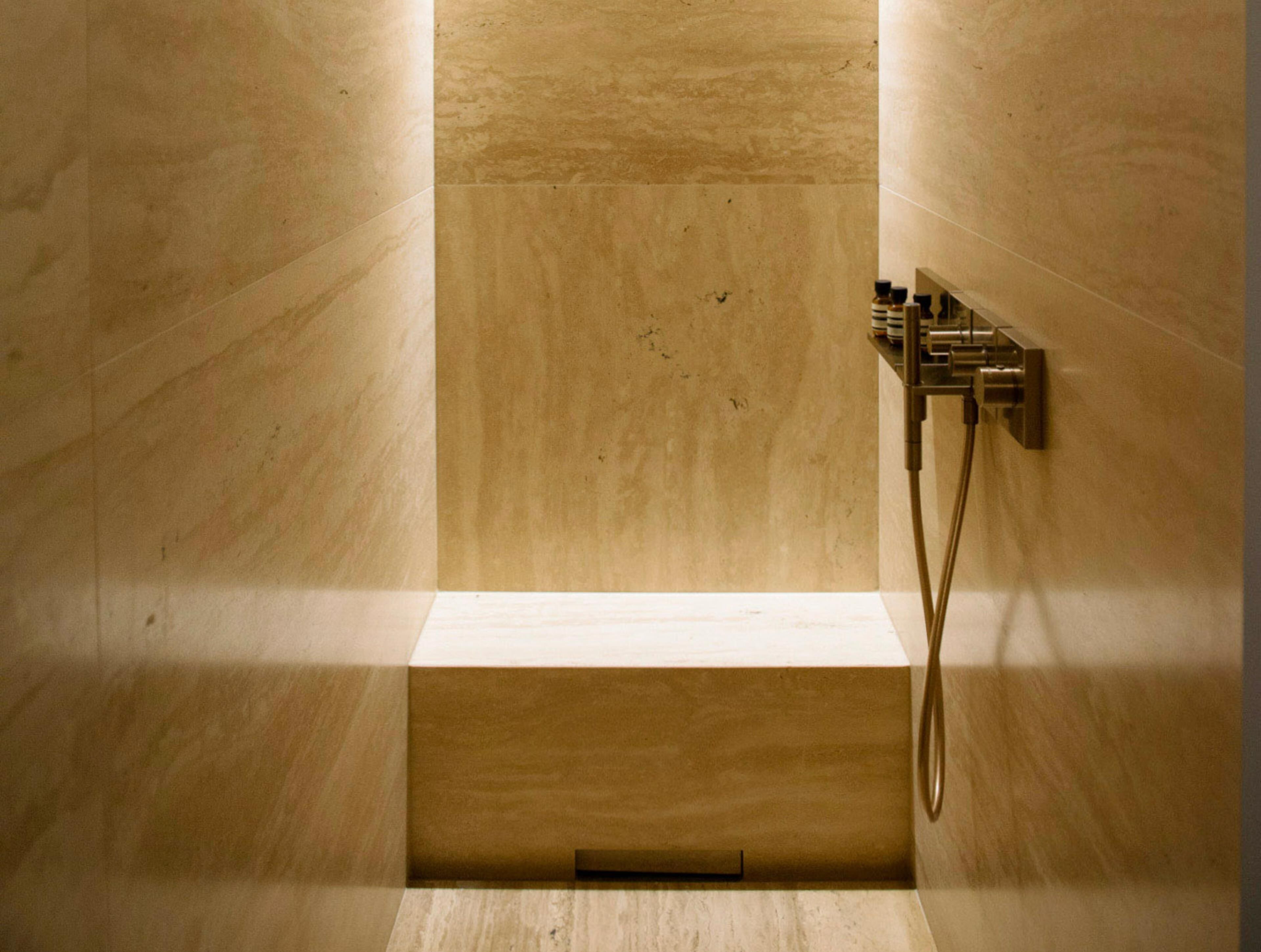 Un baño minimalista con ducha integrada, grifo de pared y plataforma de madera.