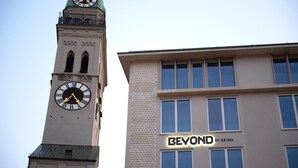 A clock tower with Roman numerals and a modern building with a 'BEYOND BY GEISEL' sign. - BEYOND by Geisel (Munich)