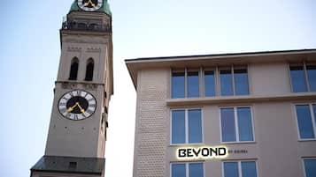 Une tour de l’horloge ornée de chiffres romains et un bâtiment moderne portant l’inscription « BEYOND BY GEISEL ».