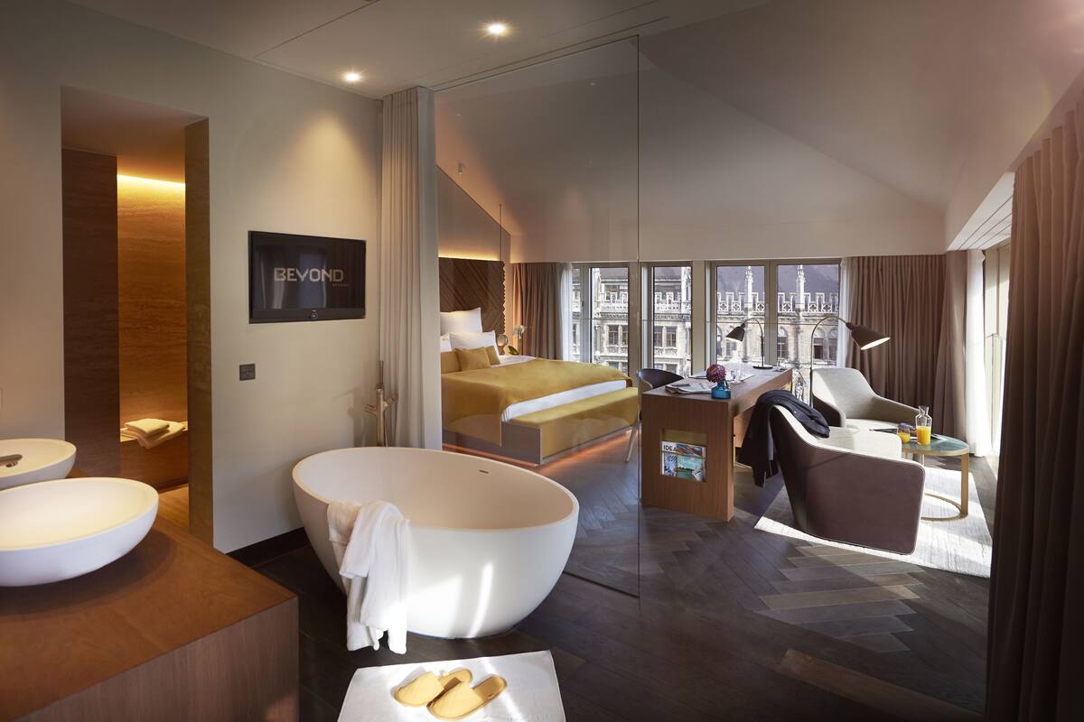 Et moderne hotelværelse med et stort badekar, en seng med udsigt over byen, et skrivebord med stol og et stort vindue.