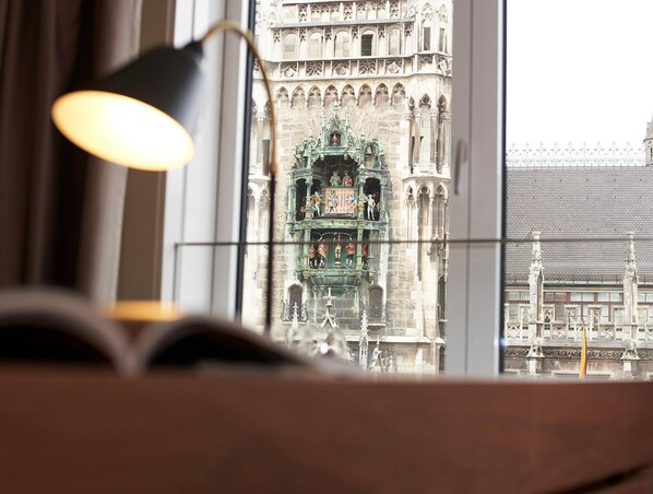 A view of a historic building with intricate architecture through a window, a lamp, and an open book. - BEYOND by Geisel (Munich)
