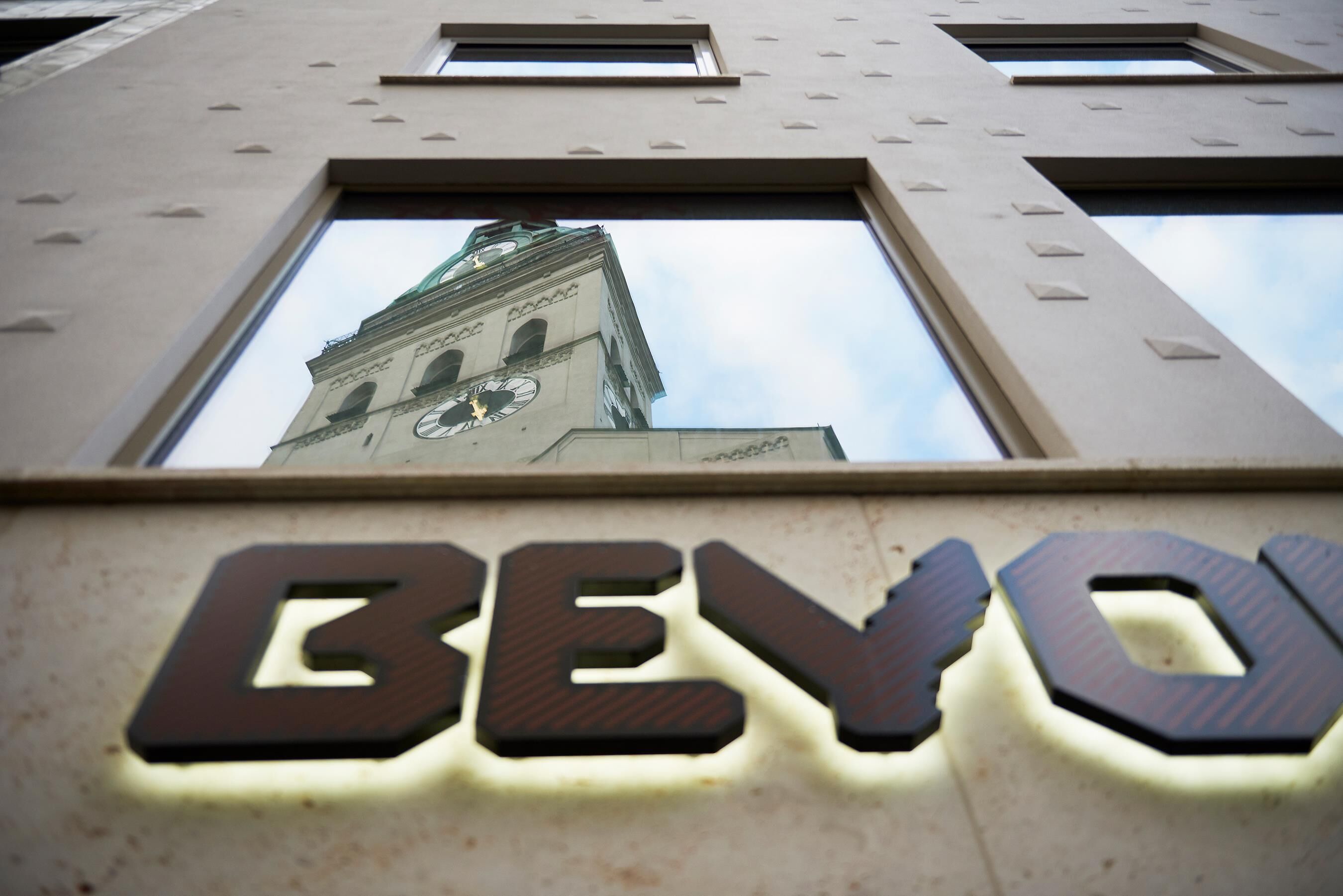 Un bâtiment doté d’une tour horlogère et dont la façade est illuminée par le mot « BEVO ».