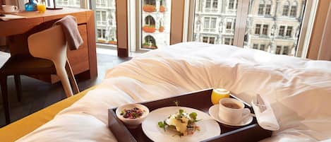 A hotel room with a bed, a desk, a chair, a tray with breakfast items, and a newspaper.