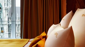 A hotel room with a view of a historic building, a window with curtains, and a bed with pillows. - BEYOND by Geisel (Munich)