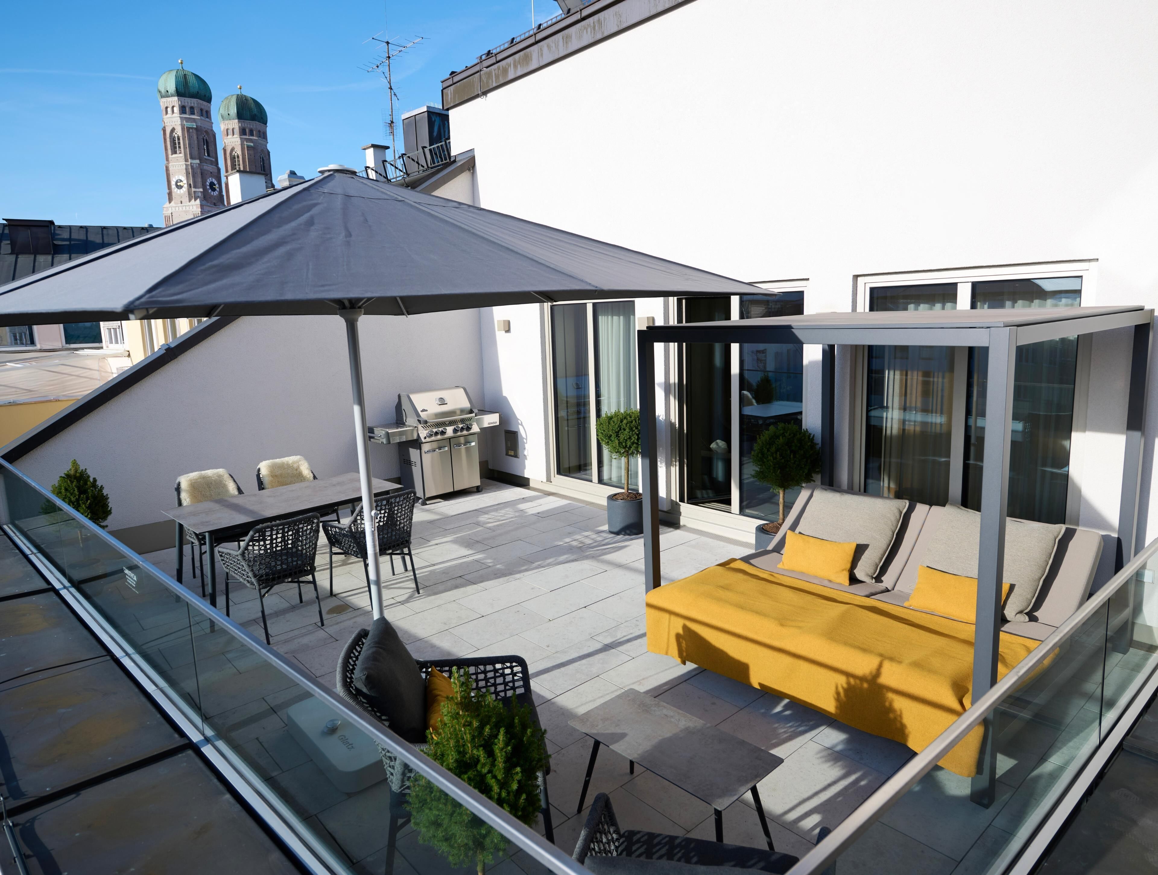 Terraza en la azotea con una parrilla, zona de estar y barandilla de cristal.