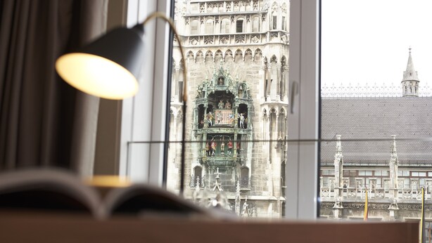 A view through a window with a lamp, showcasing a historic building with intricate architecture and a clock tower. - BEYOND by Geisel (Munich)
