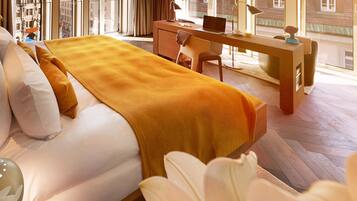 Habitación de hotel con cama, escritorio y vista a la ciudad a través de amplias ventanas.