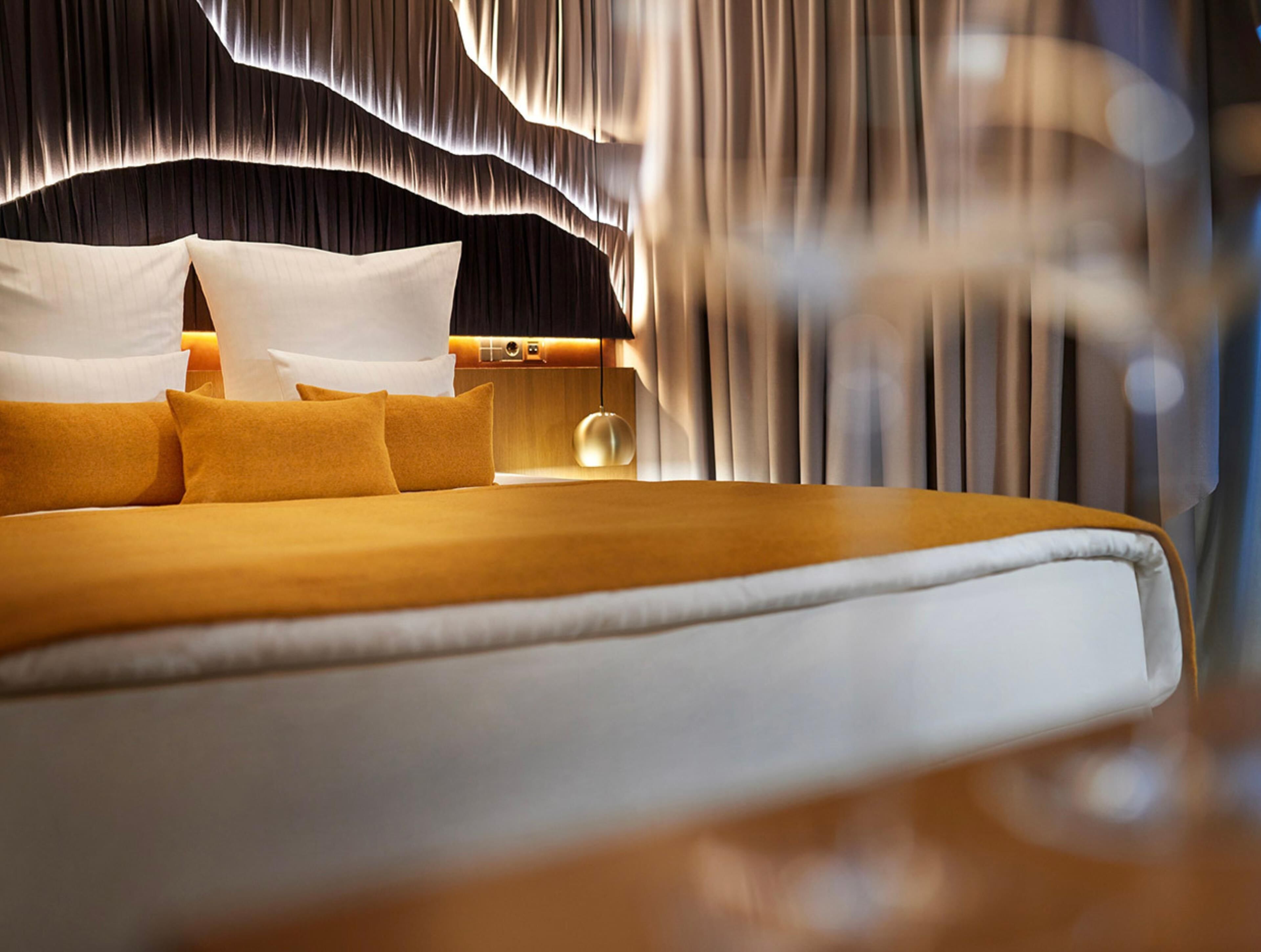A large bed with a headboard, pillows, and a bedside table with a lamp.