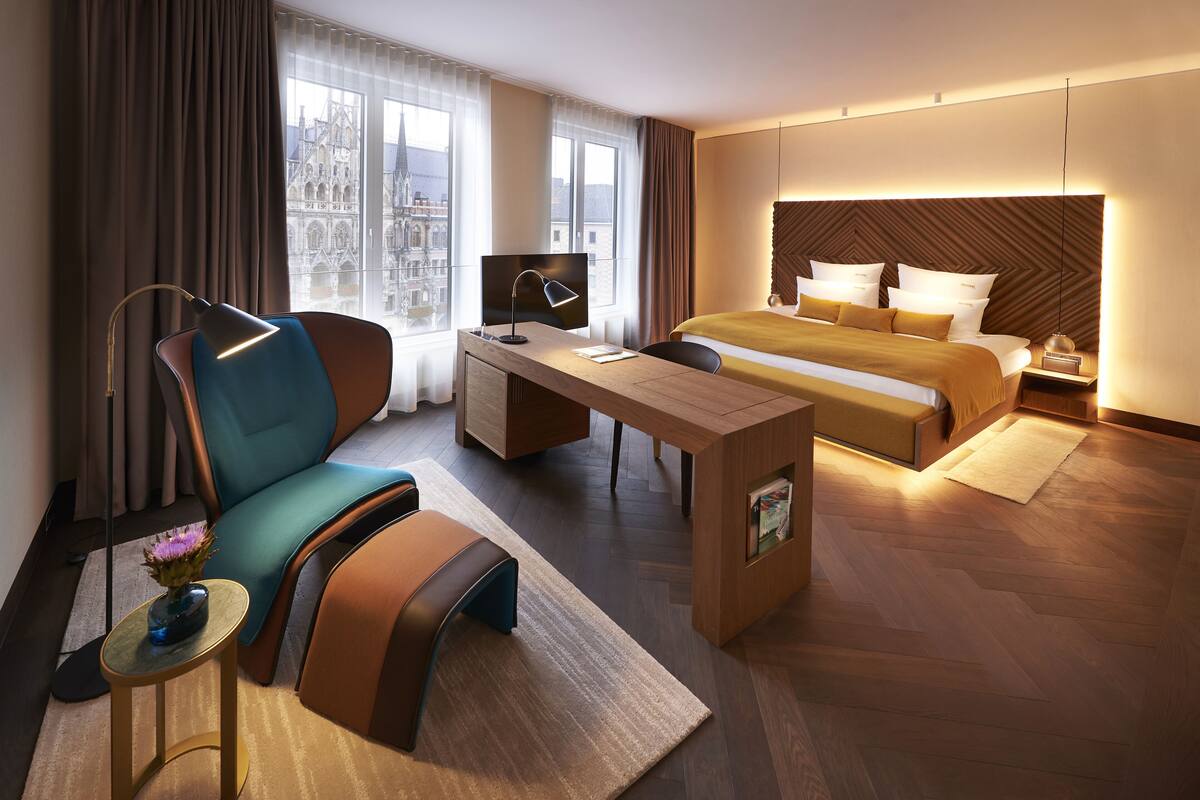 Et moderne hotelværelse med en stor seng, et skrivebord, en stol og udsigt til en historisk bygning.