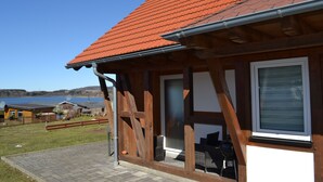 A wooden building with a red-tiled roof, a large window, and a view of a body of water. - HM- Holiday home 1 Deluxe Krombachtalsperre (Driedorf)
