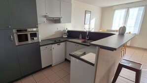 A modern kitchen with grey cabinets, stainless steel appliances, a built-in oven, and a small island with a sink and stools.