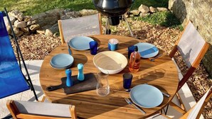 Una mesa de madera redonda preparada para cuatro, con platos azules, un bol de madera y una botella de licor.