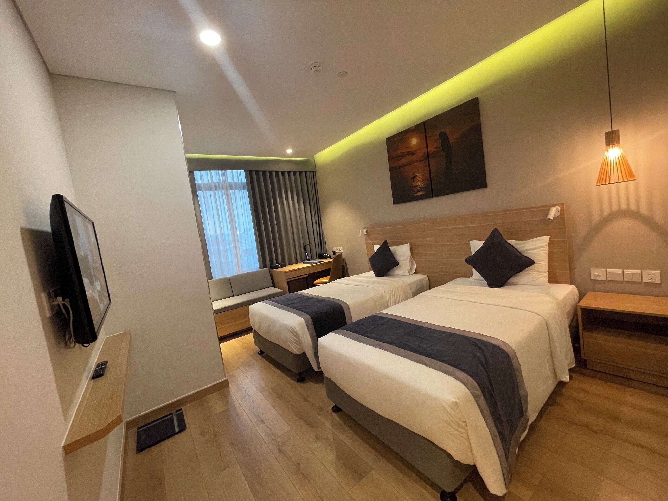 A hotel room with two beds, a desk, a chair, a TV, and a window with curtains.