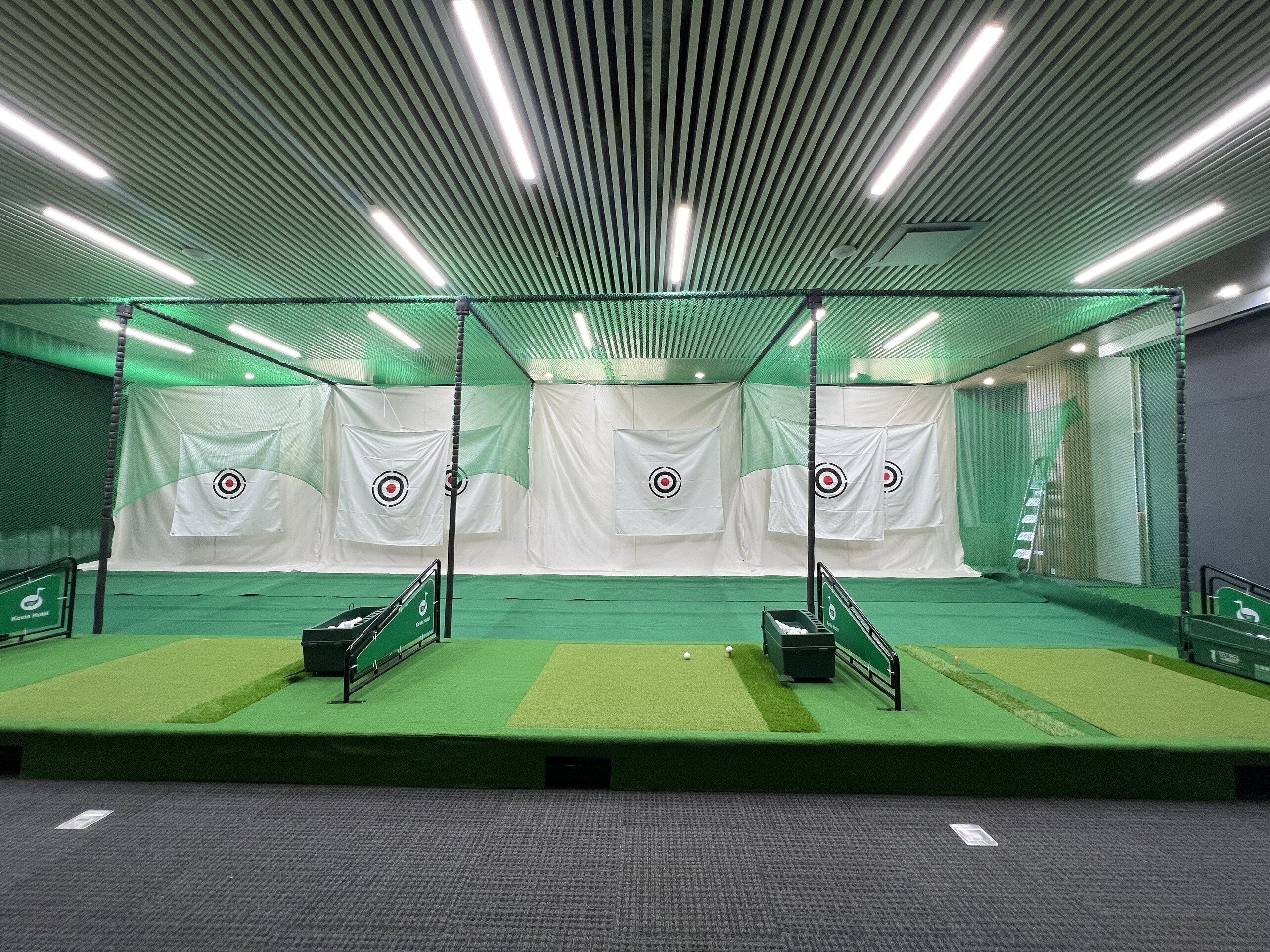 A batting cage with netting, targets, and a green turf floor.