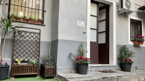 Ein Gebäude mit grau-weißer Fassade, einer Holzbank, Pflanzkübeln und einem kleinen Garten.