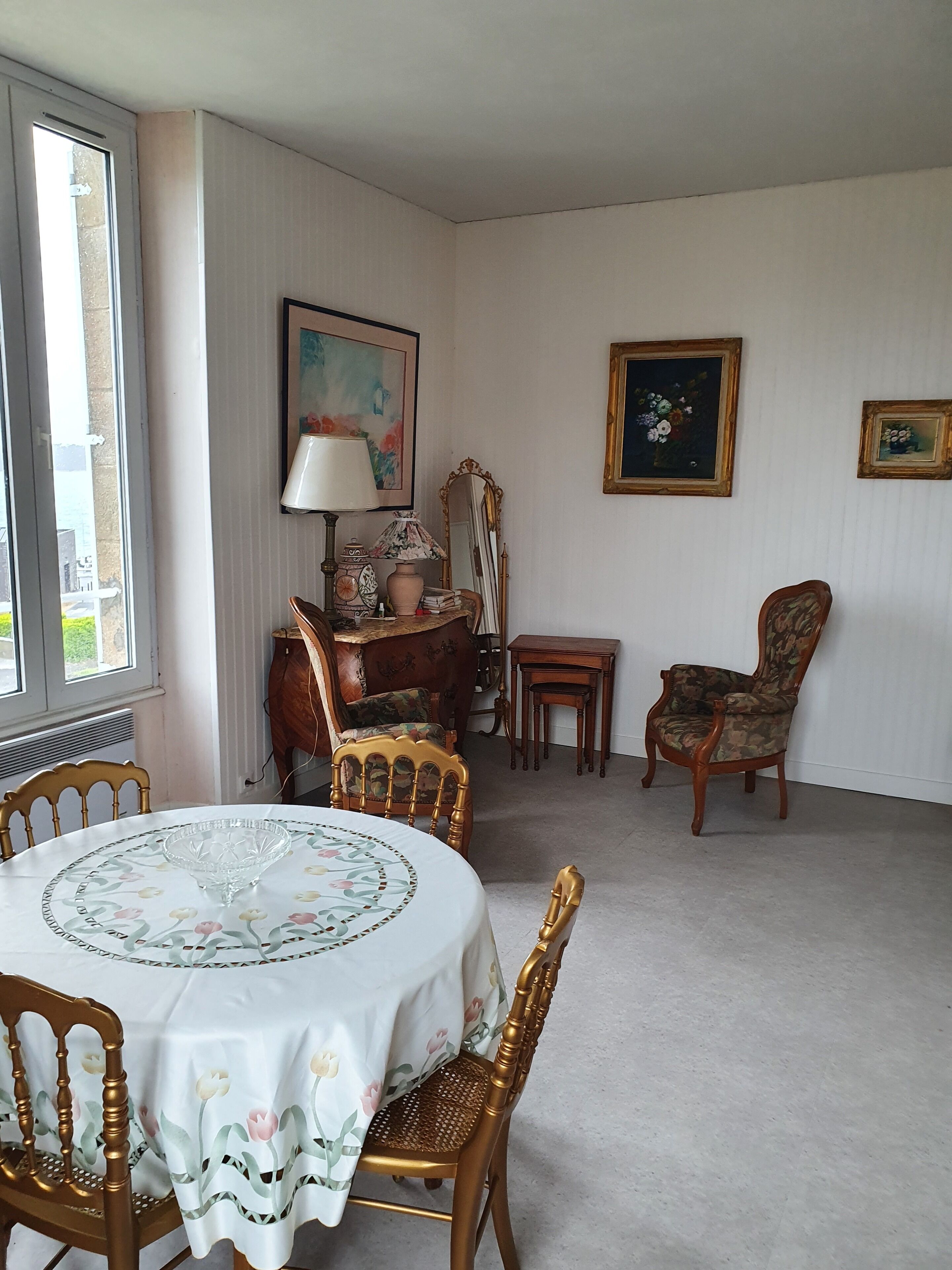 A dining area with a round table, chairs, a lamp, a mirror, and framed artwork on the walls.