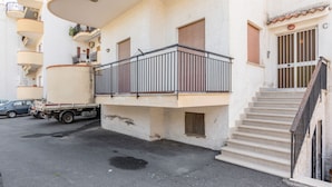 A multi-story building with balconies, a truck parked in front, and a staircase leading to the entrance. - GuestHost - Cozy 60 sqm apartment, for 4 people, with two bedroom, a terrace and a balcony, located on the 4th floor of a building with no lift. The property is located in a strategic position in Giardini Naxos, a seaside area near Taormina, less than 10 (Giardini Naxos)