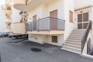 Un edificio a più piani con balconi, un camion parcheggiato davanti e una scala che conduce all'ingresso.