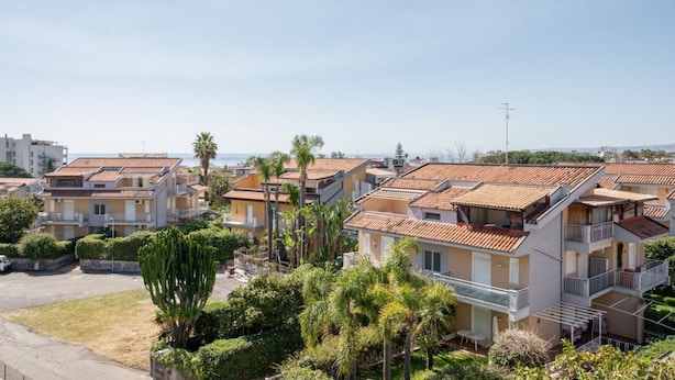 A coastal residential area with terraced houses, balconies, and a clear view of the sea. - GuestHost - Cozy 60 sqm apartment, for 4 people, with two bedroom, a terrace and a balcony, located on the 4th floor of a building with no lift. The property is located in a strategic position in Giardini Naxos, a seaside area near Taormina, less than 10 (Giardini Naxos)
