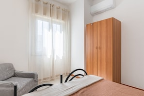 Una camera da letto con un letto, un divano grigio, un armadio in legno e una finestra con tende leggere.
