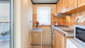 A compact kitchen with a gas stove, oven, microwave, and a small table with a vase. - GuestHost - Cozy 60 sqm apartment, for 4 people, with two bedroom, a terrace and a balcony, located on the 4th floor of a building with no lift. The property is located in a strategic position in Giardini Naxos, a seaside area near Taormina, less than 10 (Giardini Naxos)