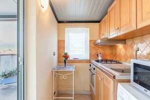 Una cucina compatta con piano cottura a gas, forno, microonde e un piccolo tavolo con un vaso.