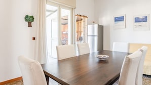 A dining area with a wooden table, white chairs, a refrigerator, and a view of the kitchen through a glass door. - GuestHost - Cozy 60 sqm apartment, for 4 people, with two bedroom, a terrace and a balcony, located on the 4th floor of a building with no lift. The property is located in a strategic position in Giardini Naxos, a seaside area near Taormina, less than 10 (Giardini Naxos)