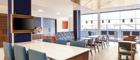 A modern dining area with a large white table, blue chairs, and a flat-screen TV mounted on the wall.