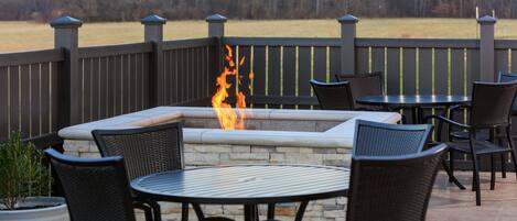 Eine Terrasse im Freien mit Feuerstelle, Sitzgelegenheiten und Blick auf ein Feld.