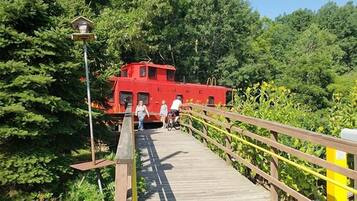 A wooden bridge leading to a red boat house surrounded by dense greenery.