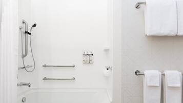 A modern bathroom with a bathtub, shower, grab bars, and white towels.