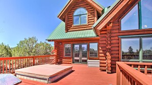A log cabin with a deck, large windows, and a green roof.