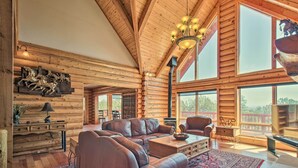 A log cabin interior with a large leather sofa, wooden walls, and a large window offering a view.