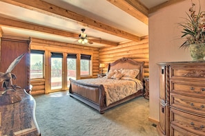 A log cabin bedroom with a bed, wooden dresser, and a ceiling fan.