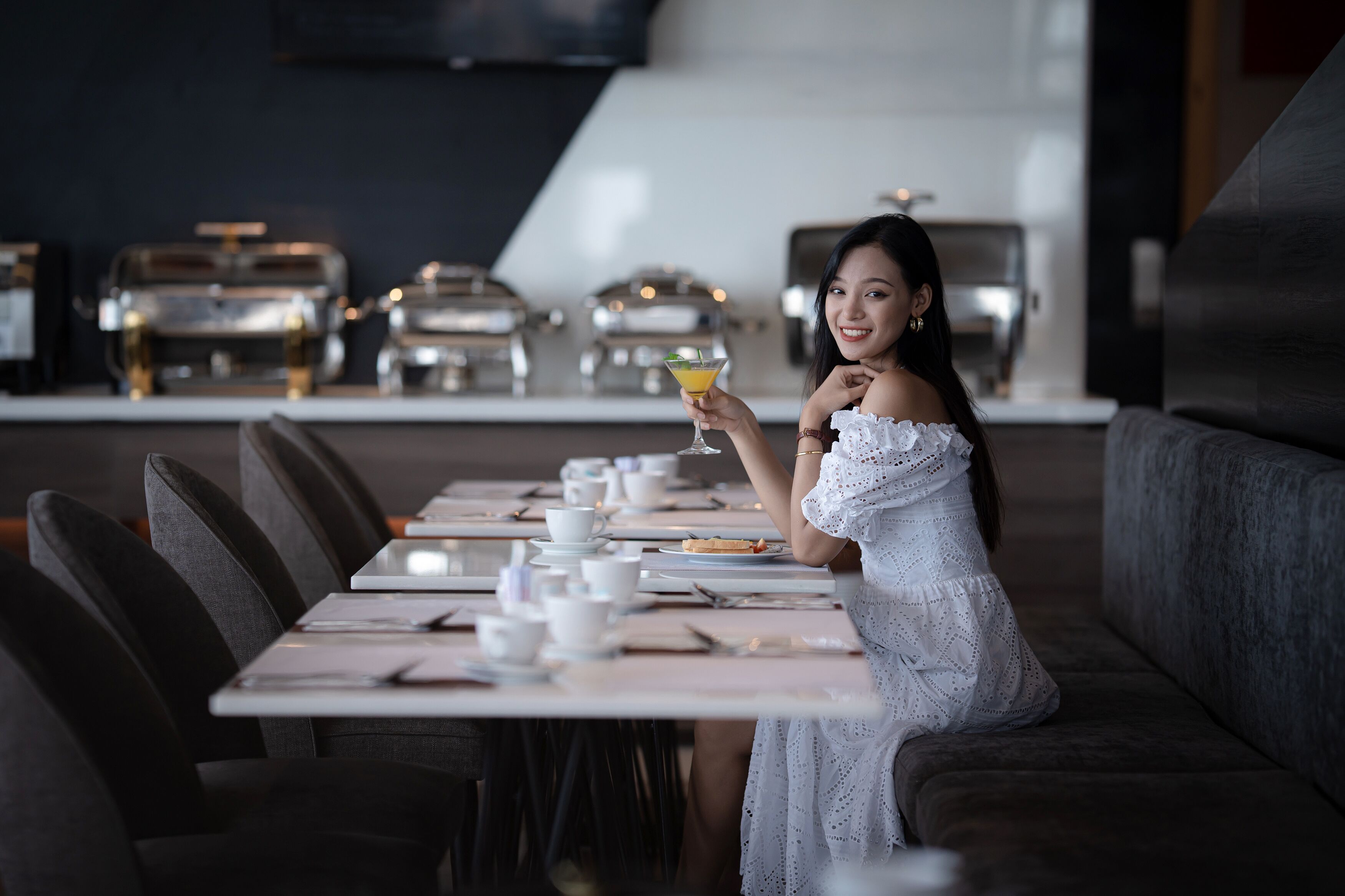 A woman seated at a table in a modern restaurant with a bar area in the background.
