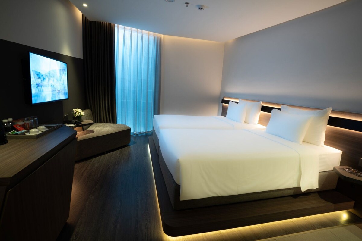 Une chambre d’hôtel moderne équipée d’un grand lit, d’un bureau, d’une télévision et d’une fenêtre avec des rideaux.