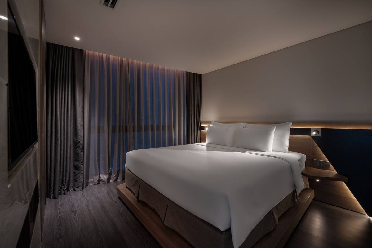 A modern hotel room with a large bed, wooden headboard, and a view of the city.