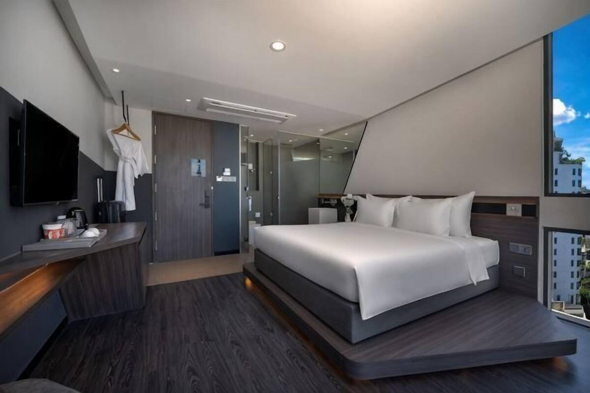 A modern hotel room with a large bed, a TV, a desk, and a view of the city.