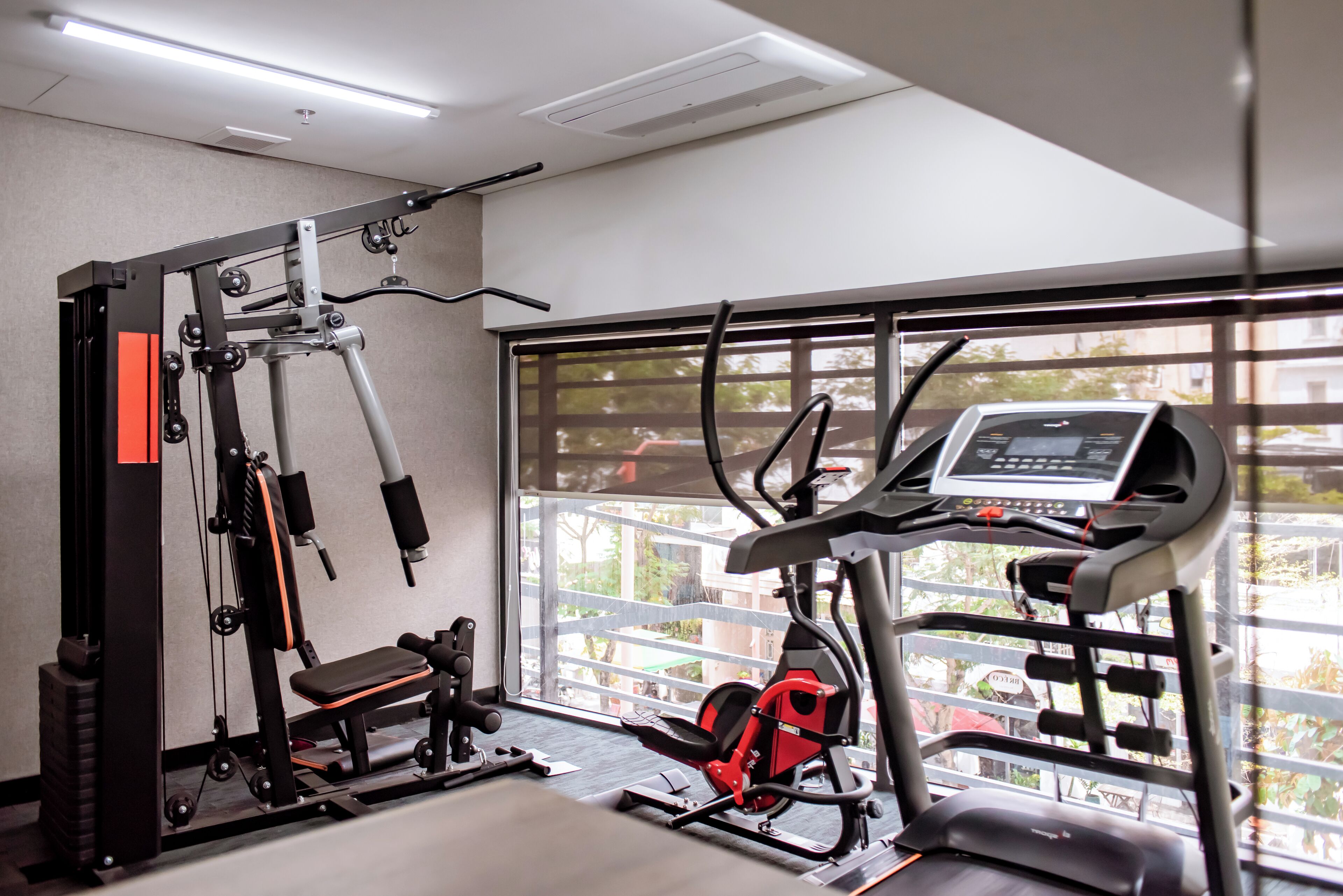 A gym with exercise equipment, a bench, and a window with a view of buildings and trees.