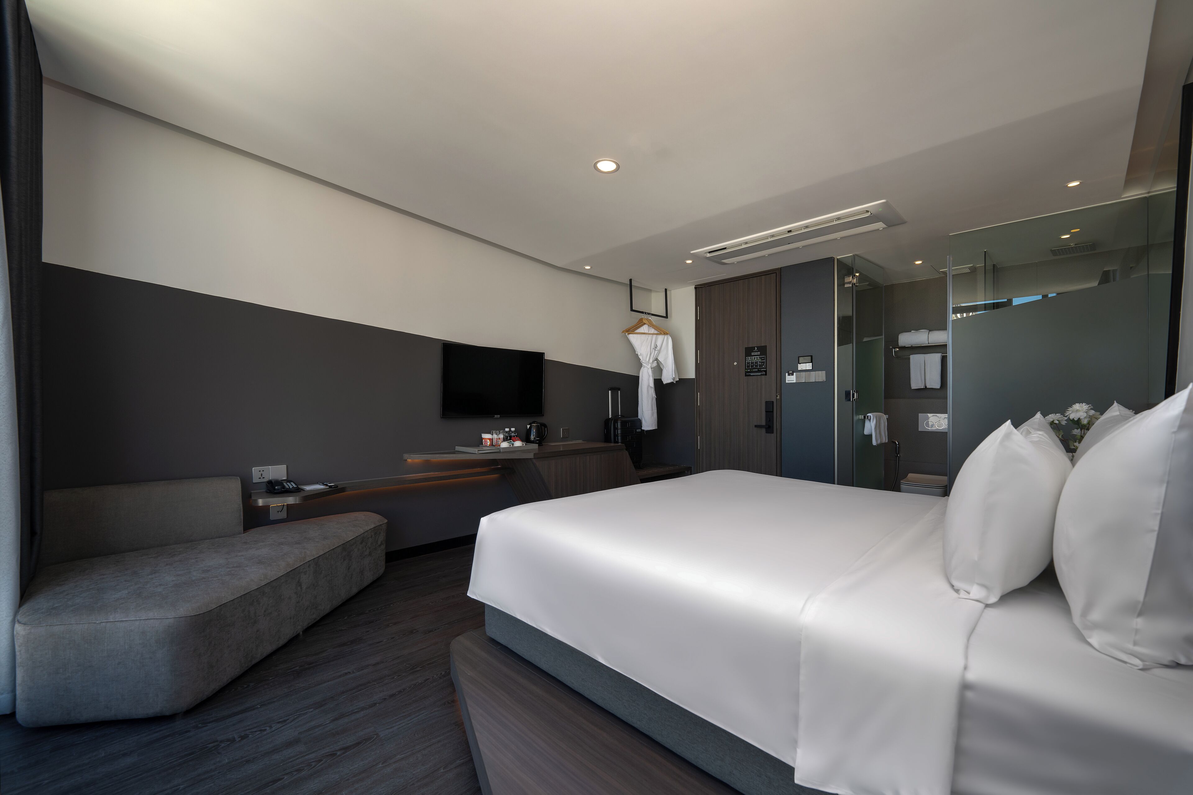 Ein modernes Hotelzimmer mit einem großen Bett, einer Sitzecke, einem Flachbildfernseher und einer Duschkabine aus Glas.