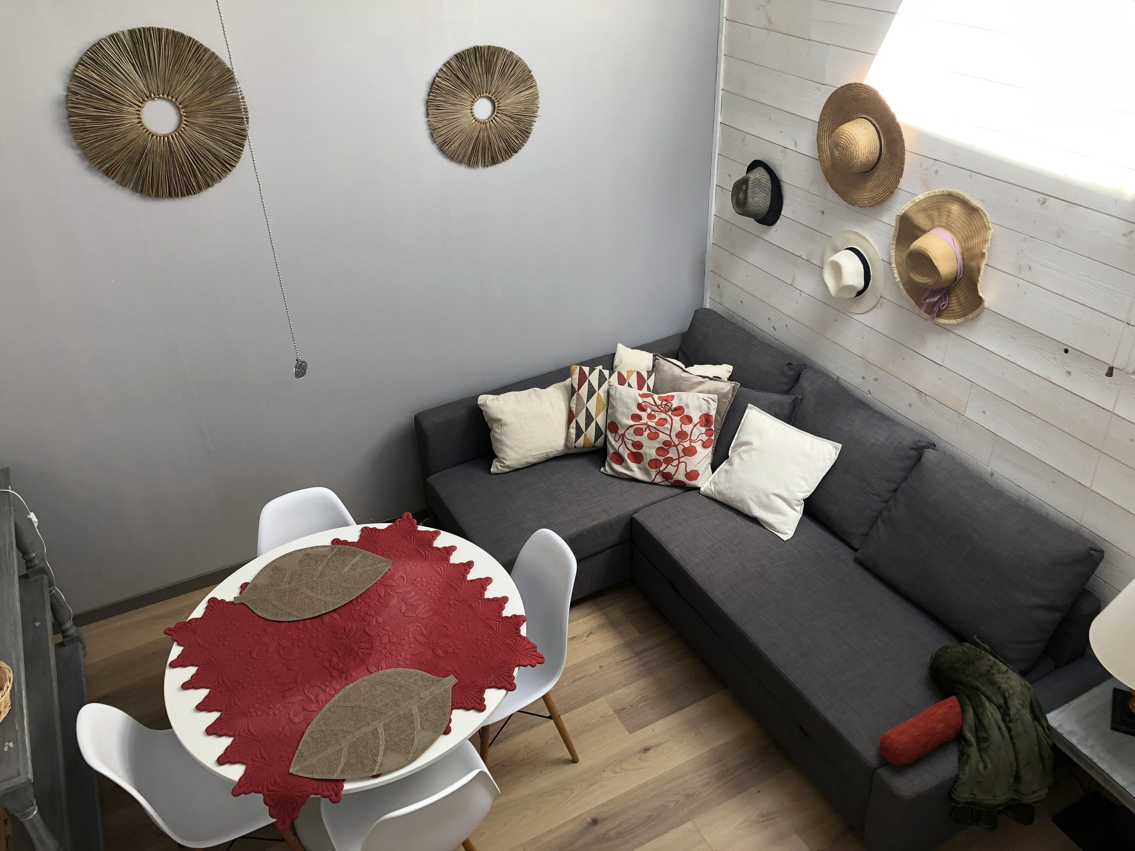 A modern living room with a grey sofa, a round table with a red leaf-patterned table runner, and a wooden floor.